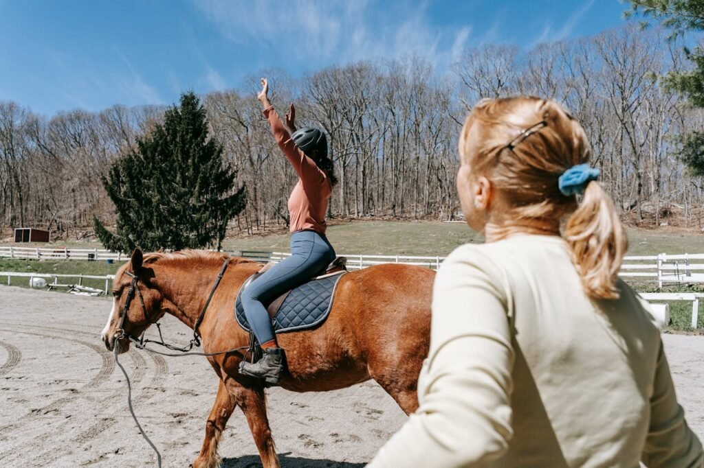 Woman learning horseback riding with an instructor in a sunny outdoor setting.