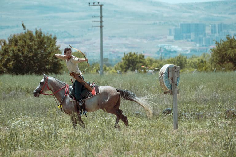 A skilled archer on horseback aiming at a target in picturesque Turkish landscape.