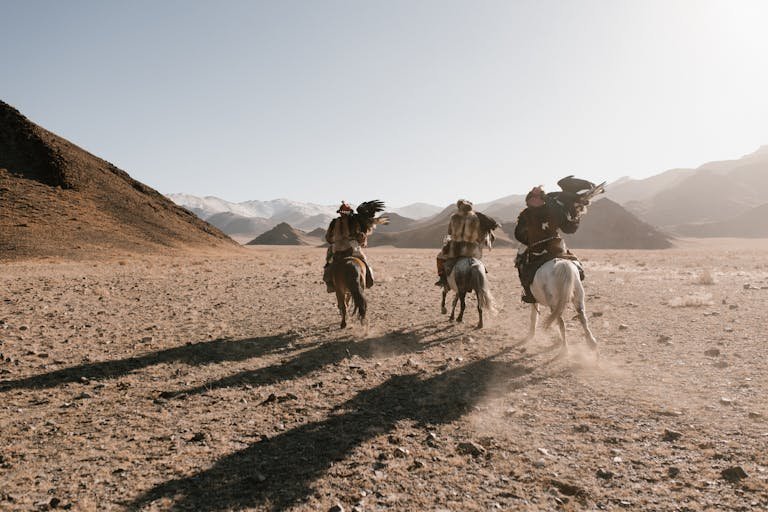 Riders in a desert landscape with eagles, showcasing traditional horsemanship.